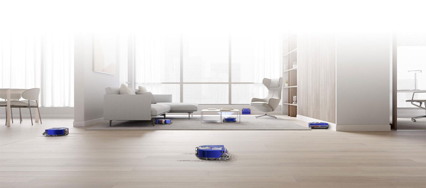 W przestronnym, nowoczesnym salonie z dużymi oknami widoczne są cztery niebieskie roboty sprzątające na podłodze. W tle znajdują się meble, takie jak sofa, fotel i stolik kawowy.