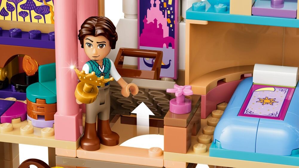 Zestaw LEGO przedstawia wnętrze zamku z figurką postaci trzymającą złoty przedmiot. W tle widoczne są łóżko z fioletową pościelą i różowe dekoracje na ścianie.