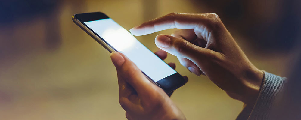 Osoba trzyma smartfon i dotyka jego ekranu, który jest jasno podświetlony.