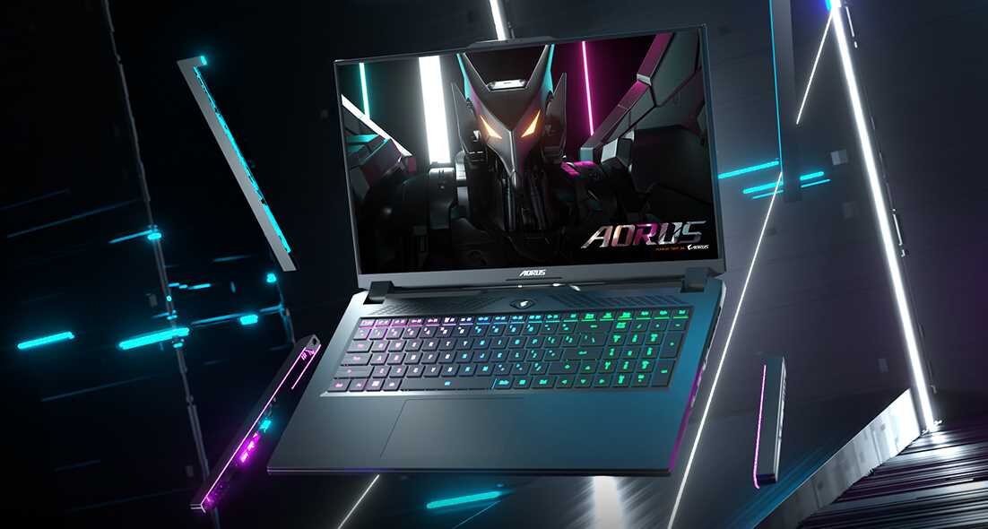 Laptop z podświetlaną klawiaturą i ekranem wyświetlającym grafikę z futurystycznym motywem. Na ekranie widoczny jest napis \'AORUS\'.