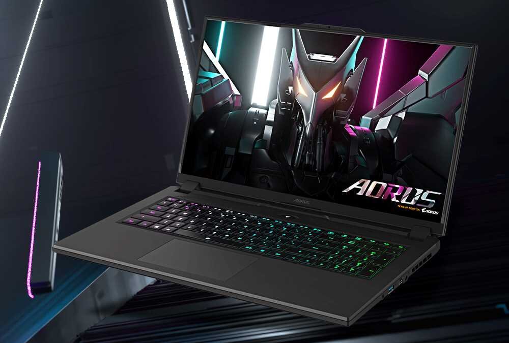 Laptop z podświetlaną klawiaturą wyświetla na ekranie grafikę z futurystycznym robotem i logo \'AORUS\'.