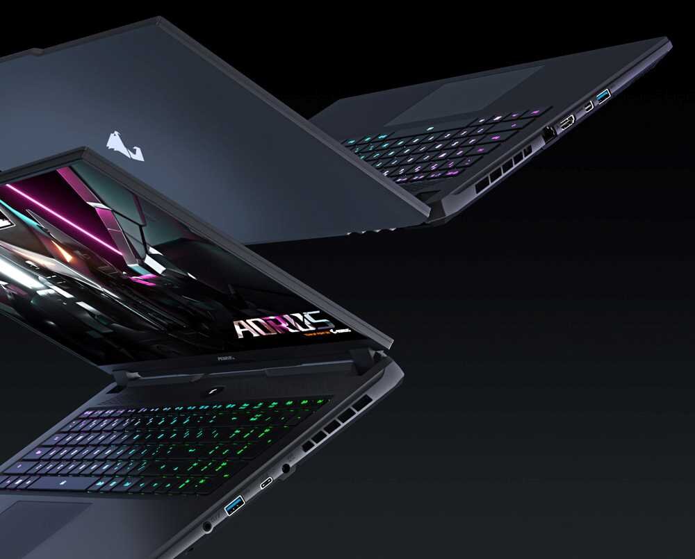 Na obrazie widoczne są dwa laptopy z podświetlanymi klawiaturami i ekranami wyświetlającymi grafikę z napisem \'AORUS\'. Na obudowie jednego z laptopów znajduje się logo producenta w kształcie ptaka.