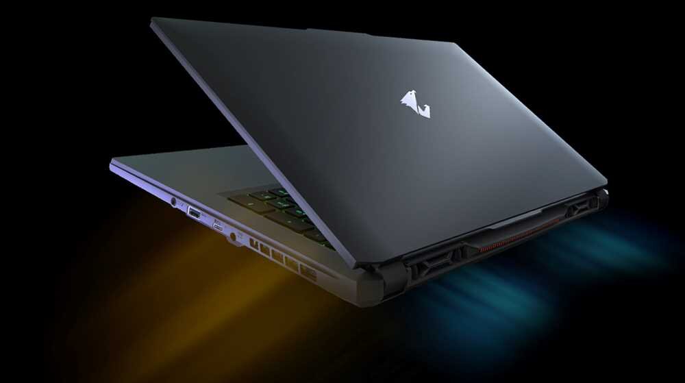 Laptop z otwartą pokrywą, widoczny z boku, z podświetlaną klawiaturą i logo w kształcie litery \'A\' na obudowie. Z tyłu laptopa widoczne są kolorowe efekty świetlne.