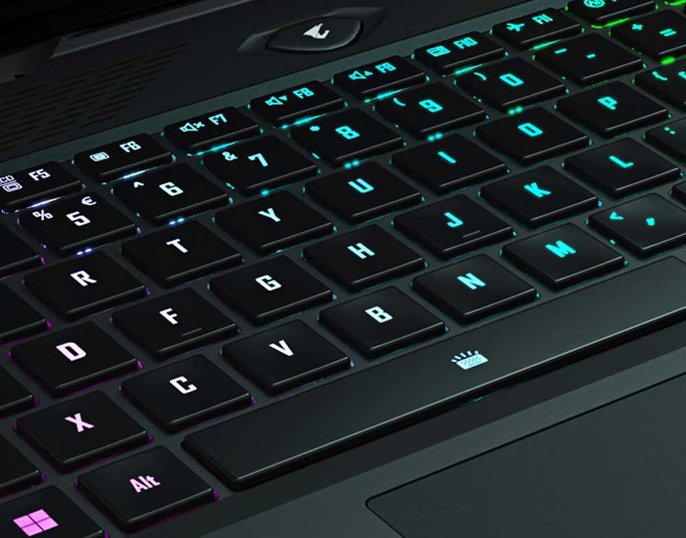 Zbliżenie na klawiaturę laptopa z podświetleniem RGB, widoczne są klawisze z literami i cyframi. Na obudowie nad klawiaturą znajduje się logo producenta w kształcie stylizowanej litery \'A\'.