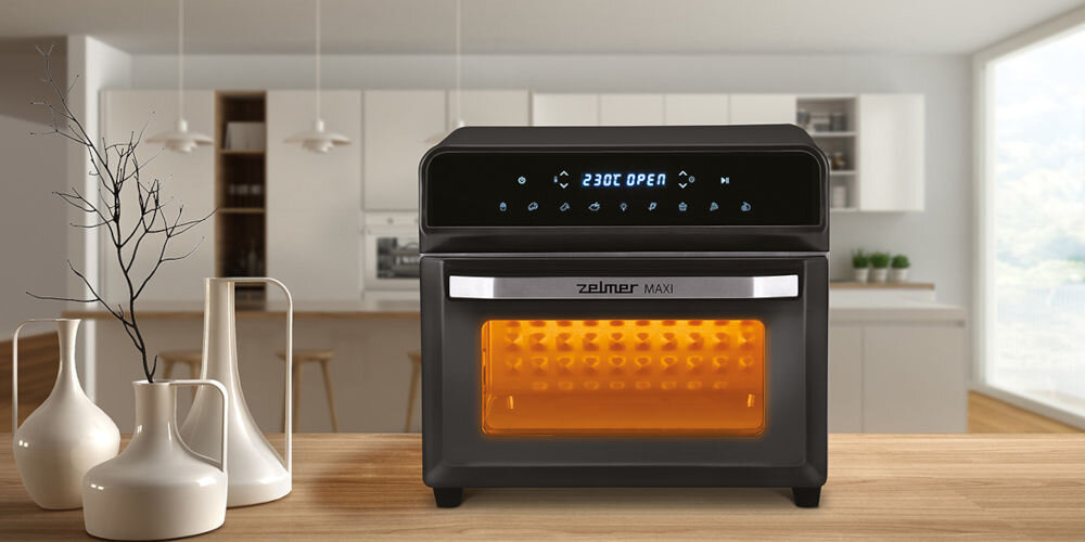 Na obrazie znajduje się frytkownica beztłuszczowa z wyświetlaczem pokazującym \'230C OPEN\'. Urządzenie ma przezroczyste okienko z pomarańczowym podświetleniem i logo \'zelmer MAXI\'.