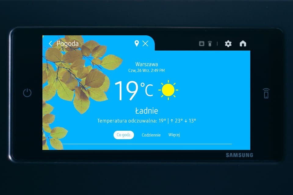 ekran pogoda Ekran urządzenia pokazuje prognozę pogody dla Warszawy z temperaturą 19°C i ikoną słońca. Widoczny jest napis \'Ładnie\' oraz logo \'SAMSUNG\'.