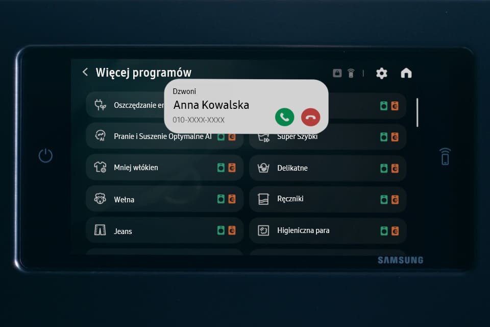 na wyświetlaczu pralko-suszarki zobaczysz, gdy ktoś zadzwoni do drzwi Ekran pralko-suszarki pokazuje listę programów, takich jak \'Oszczędzanie energii\' i \'Pranie i Suszenie Optymalne AI\'. Na ekranie widoczna jest także informacja o przychodzącym połączeniu od \'Anna Kowalska\'.