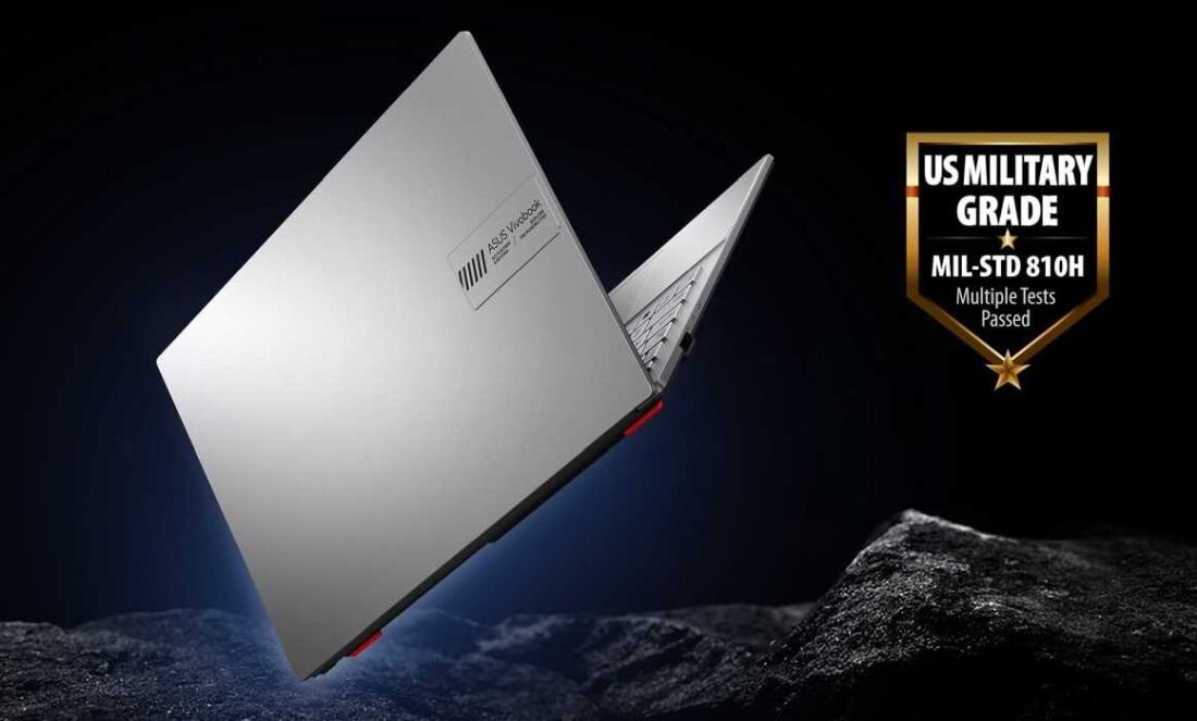 Srebrny laptop z widocznym logo ASUS VivoBook unosi się nad powierzchnią przypominającą skały. Obok znajduje się odznaka z napisem \'US MILITARY GRADE MIL-STD 810H Multiple Tests Passed\'.