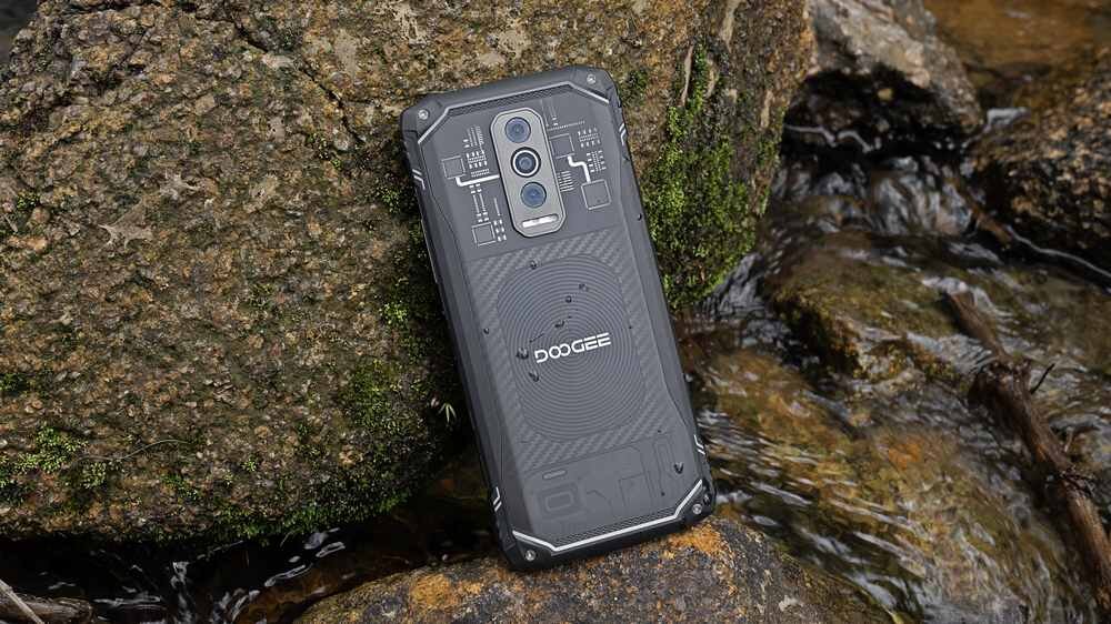Smartfon z widocznym logo \'DOOGEE\' leży na kamieniach przy strumieniu. Obudowa telefonu ma wzór przypominający obwody elektroniczne.