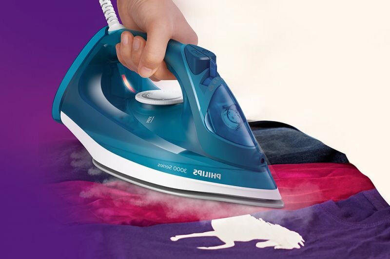 Osoba prasuje kolorową tkaninę żelazkiem w kolorze niebieskim z napisem \'PHILIPS 3000 Series\'. Z żelazka wydobywa się para, a na tkaninie widoczny jest biały kształt konia.