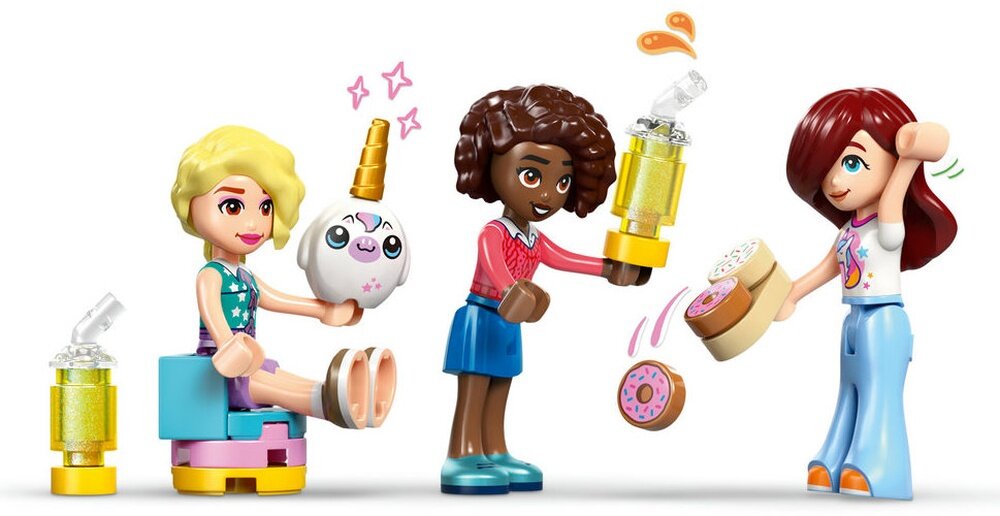 Trzy figurki LEGO przedstawiające postacie w kolorowych ubraniach, trzymające akcesoria takie jak kubki i ciastka. Jedna z figurek trzyma okrągły przedmiot z rysunkiem jednorożca.