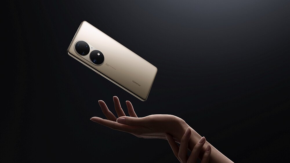 Na obrazie widać smartfon w kolorze złotym z dwoma dużymi obiektywami aparatu, unoszący się nad dłonią. Na obudowie widoczne jest logo \'HUAWEI\'.