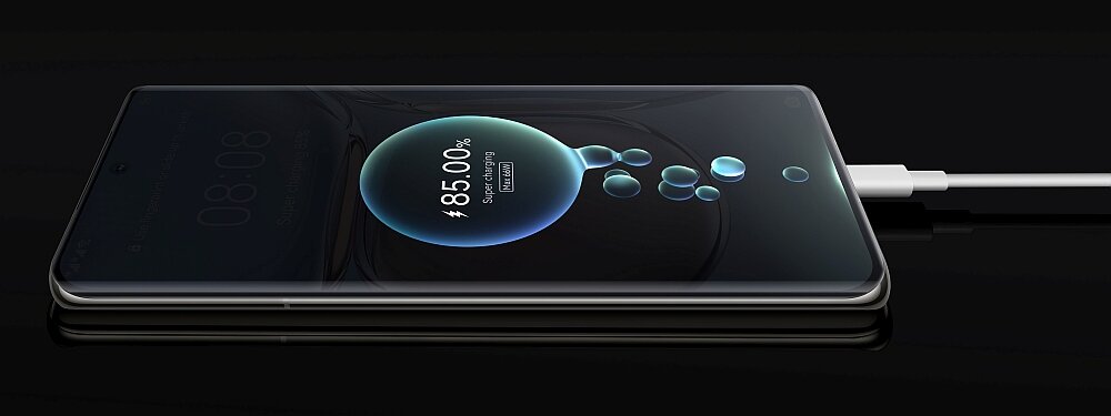Smartfon leży na płaskiej powierzchni, podłączony do ładowarki, z wyświetlaczem pokazującym stan naładowania 85,0% i napis \'SuperCharge\'.