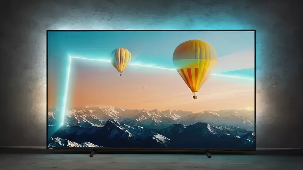 Telewizor wyświetla obraz z dwoma balonami unoszącymi się nad górskim krajobrazem. W tle widać efekt świetlny Ambilight na ścianie.