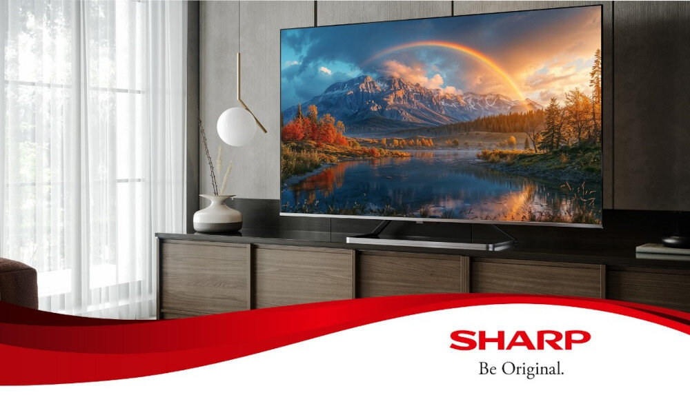 Telewizor wyświetla krajobraz z górami i jeziorem, a na dole widoczne jest logo SHARP z napisem \'Be Original.\'.