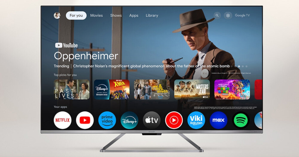 Telewizor wyświetla ekran główny z aplikacjami takimi jak Netflix, Prime Video, Disney+, Apple TV, YouTube i inne. Na ekranie widoczny jest film \'Oppenheimer\' oraz różne ikony aplikacji multimedialnych.