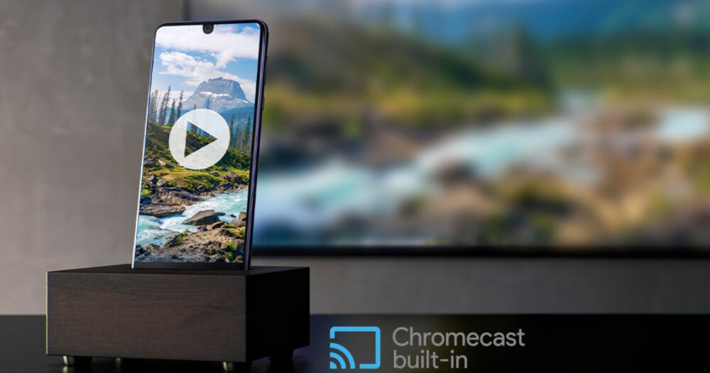 Smartfon stoi na drewnianej podstawce, na ekranie widoczny jest krajobraz górski z ikoną odtwarzania. W prawym dolnym rogu znajduje się napis \'Chromecast built-in\'.