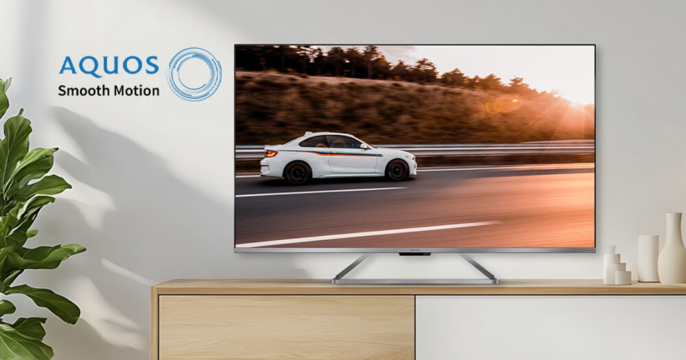 Telewizor wyświetla obraz samochodu jadącego po autostradzie o zachodzie słońca. Obok telewizora widoczne jest logo \'AQUOS Smooth Motion\'.