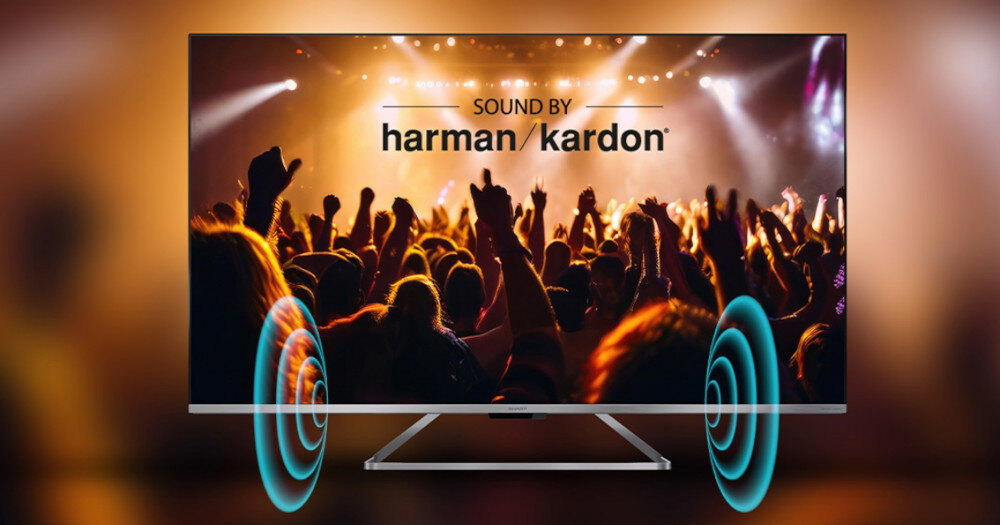 Telewizor wyświetla obraz koncertu z tłumem ludzi i efektami świetlnymi. Na ekranie widoczny jest napis \'SOUND BY harman/kardon\'.