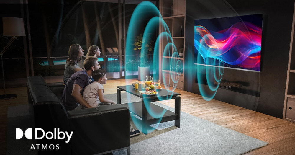 Grupa osób siedzi na kanapie w salonie, oglądając telewizor z kolorowym wyświetlaczem. W lewym dolnym rogu widoczne jest logo \'Dolby Atmos\'.