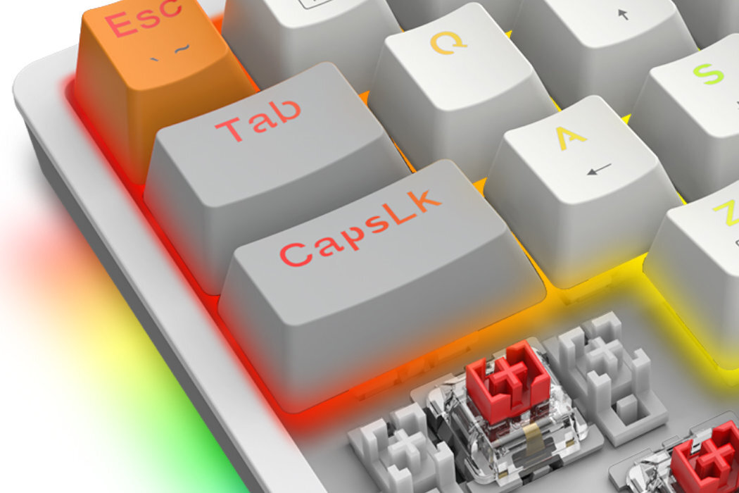 Zbliżenie na klawiaturę z klawiszami oznaczonymi jako Esc, Tab, CapsLk, Q, A, S, z podświetleniem RGB. Widoczny jest mechanizm przełącznika klawisza z czerwonym elementem.