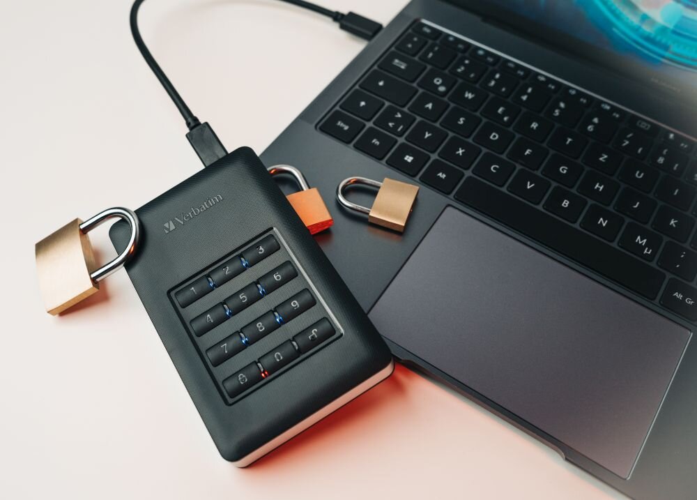 VERBATIM Store 'n' Go Secure Czarny dysk przenośny z klawiaturą numeryczną podłączony do laptopa, obok dwa kłódki, opis
