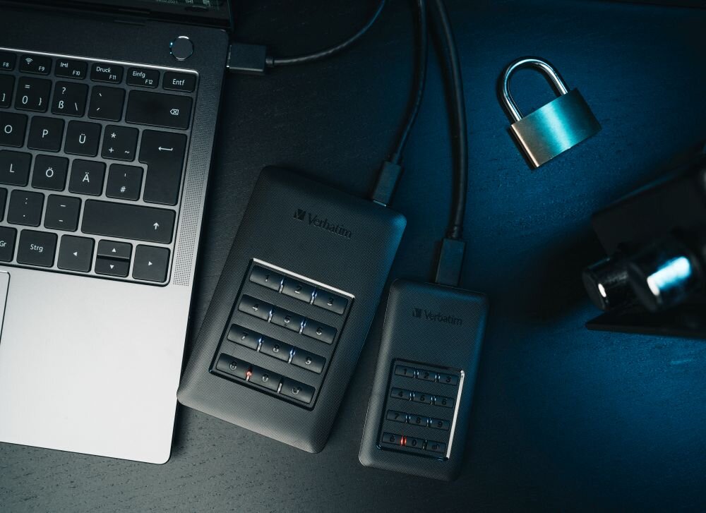 VERBATIM Store 'n' Go Secure Dwa czarne dyski przenośne z klawiaturami numerycznymi podłączone do laptopa, obok metalowa kłódka, bezpieczne przechowywanie plików