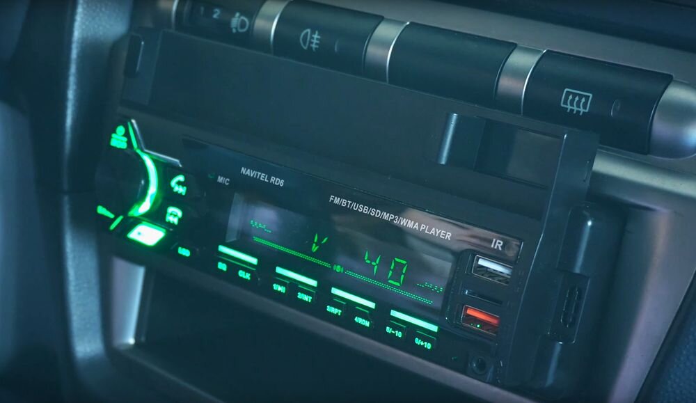 Radio samochodowe z wyświetlaczem pokazującym poziom głośności \'40\' i zielonym podświetleniem przycisków. Widoczny napis: \'NAVITEL RD6 FM/BT/USB/SD/MP3/WMA PLAYER\'.