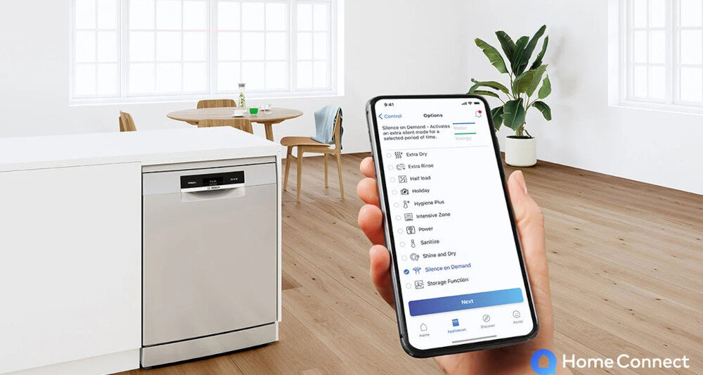 W jasnym pomieszczeniu znajduje się zmywarka z panelem sterowania, obok której osoba trzyma smartfon z aplikacją Home Connect. Na ekranie telefonu widoczne są opcje związane z funkcjami zmywarki.