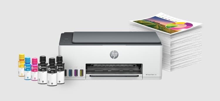 Na obrazie znajduje się urządzenie wielofunkcyjne z logo HP, obok którego stoją butelki z tuszem w różnych kolorach oraz stos papieru z kolorowym wydrukiem na wierzchu. Na urządzeniu widoczny jest napis \'HP Smart Tank 580\'.