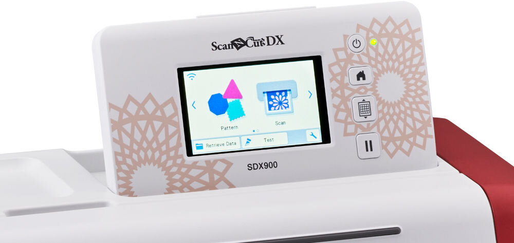 Na zdjęciu widoczny jest ekran urządzenia z napisem \'ScanNCut DX\' oraz \'SDX900\', na którym wyświetlane są kolorowe ikony i opcje menu. Obok ekranu znajdują się przyciski funkcyjne z symbolami, a tło zdobi wzór geometryczny.