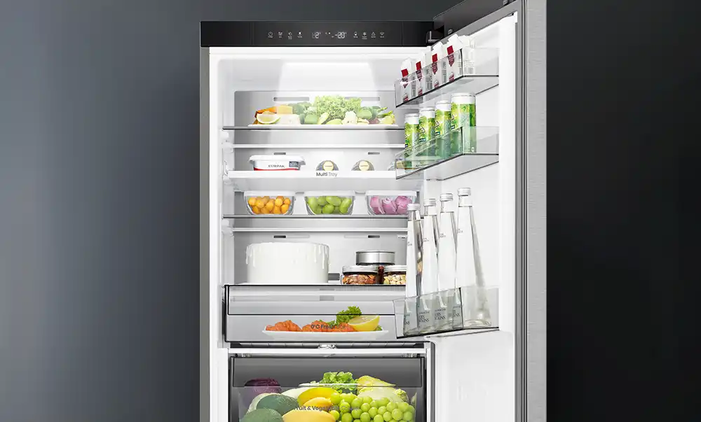 Wnętrze lodówki z kilkoma półkami, na których znajdują się różne produkty spożywcze, takie jak owoce, warzywa i napoje. Na drzwiach lodówki umieszczone są butelki i kartony z napojami.