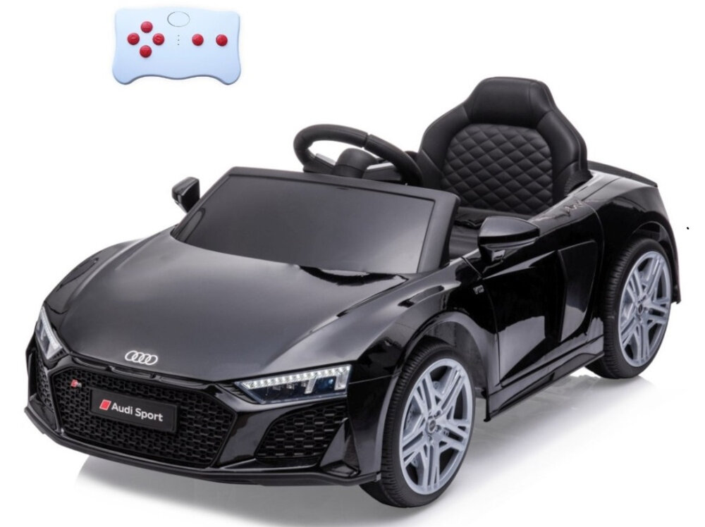 Czarny dziecięcy samochód elektryczny stylizowany na sportowy model z logo Audi na przodzie. Obok znajduje się biały pilot z czerwonymi przyciskami.