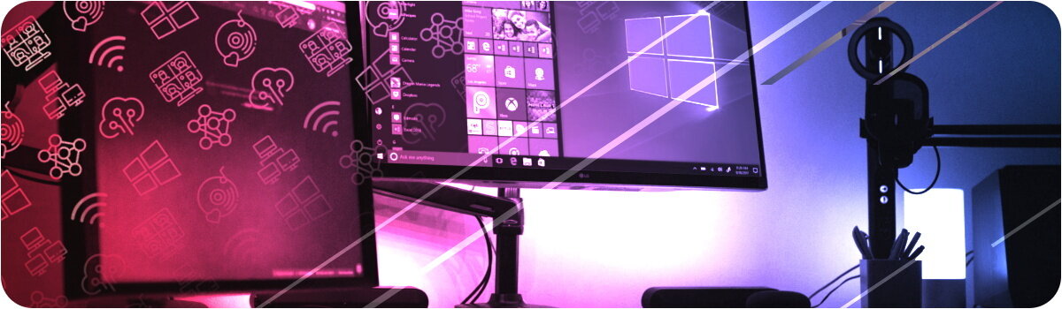 Obraz przedstawia dwa monitory na biurku, z których jeden wyświetla ekran startowy systemu Windows. W tle widoczne są różowe i niebieskie światła oraz ikony związane z technologią.
