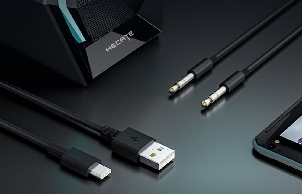 Na obrazie widoczne są kable z różnymi końcówkami, w tym USB i mini-jack, oraz fragment urządzenia z napisem \'HECATE\'. Obok znajduje się część smartfona.