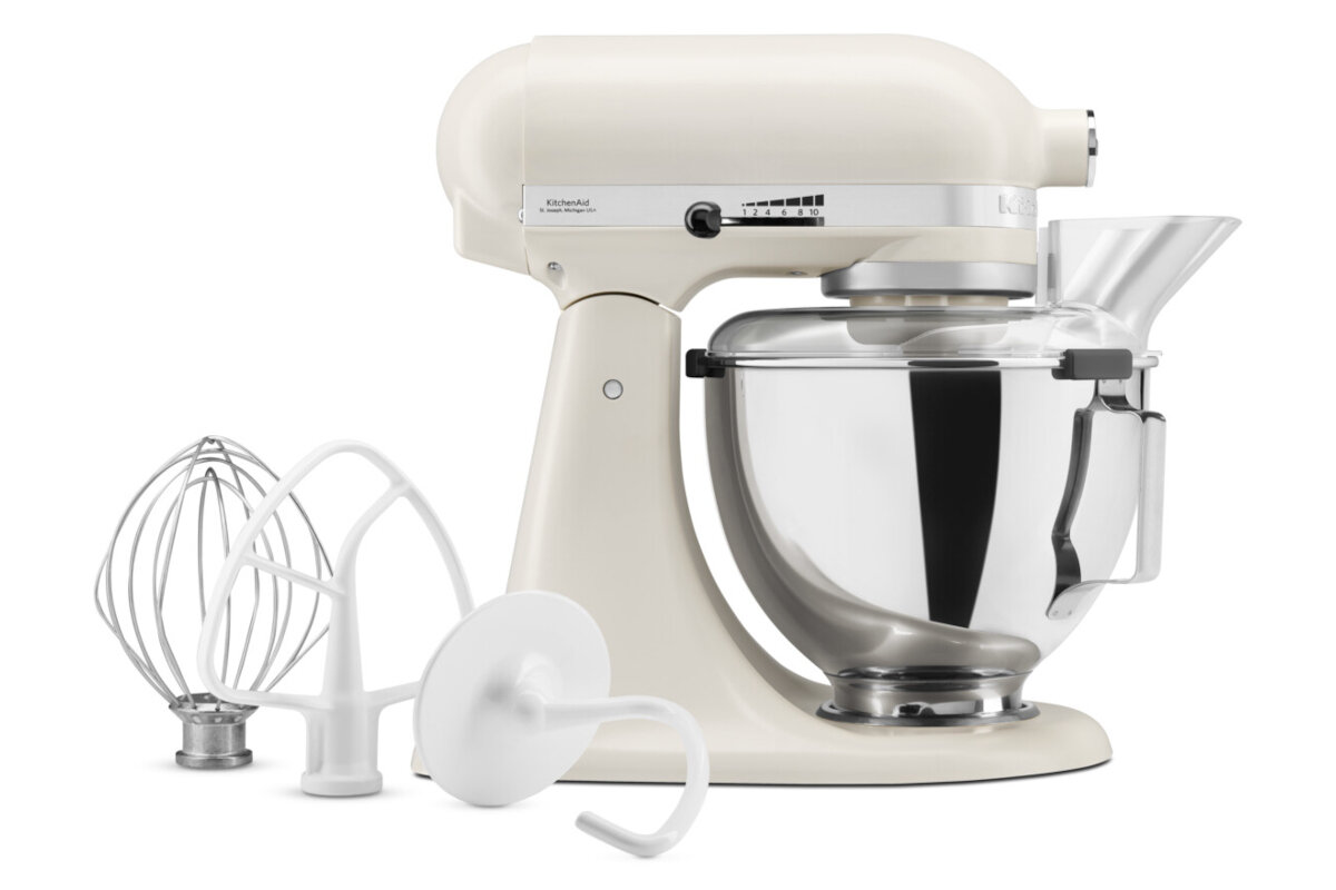 Robot kuchenny w kolorze porcelanowym z metalową misą i trzema końcówkami: trzepaczką, mieszadłem i hakiem do ciasta. Na obudowie widoczne jest logo \'KitchenAid\'.
