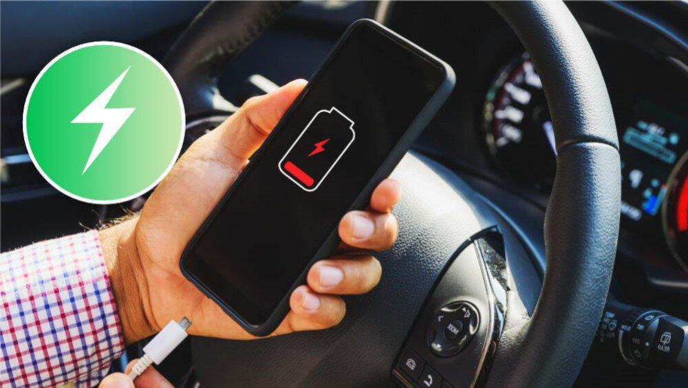 Osoba trzyma smartfon z ikoną niskiego poziomu baterii na ekranie, siedząc za kierownicą samochodu. Obok widoczna jest ikona ładowania na zielonym tle.