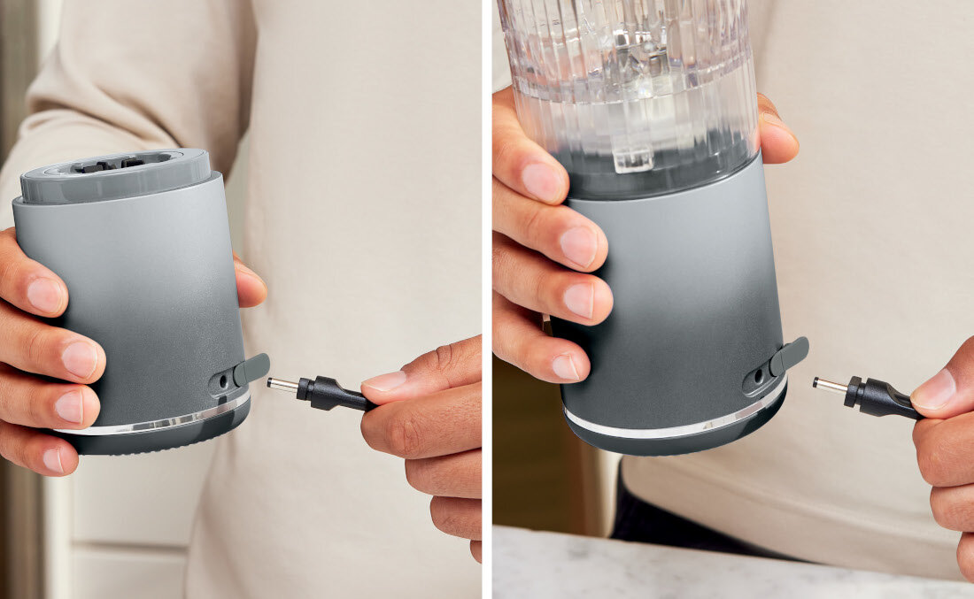 Osoba trzyma blender z szarym korpusem, do którego podłączany jest kabel zasilający. Blender ma przezroczysty pojemnik na górze.