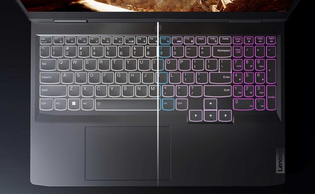 Obraz przedstawia klawiaturę laptopa z podświetleniem RGB, z widocznym logo \'Lenovo\' na obudowie. Klawisze są podświetlone w różnych kolorach, a touchpad znajduje się poniżej klawiatury.