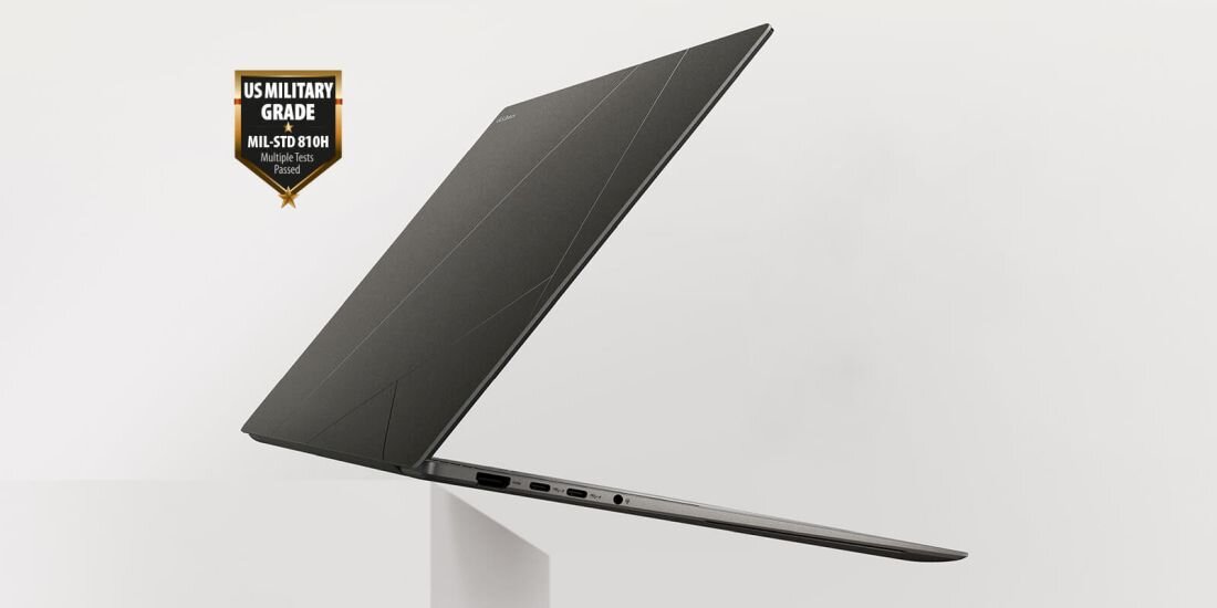 Laptop w kolorze ciemnym, widoczny z boku, z kilkoma portami na krawędzi. Obok laptopa znajduje się odznaka z napisem \'US MILITARY GRADE MIL-STD 810H Multiple tests Passed\'.