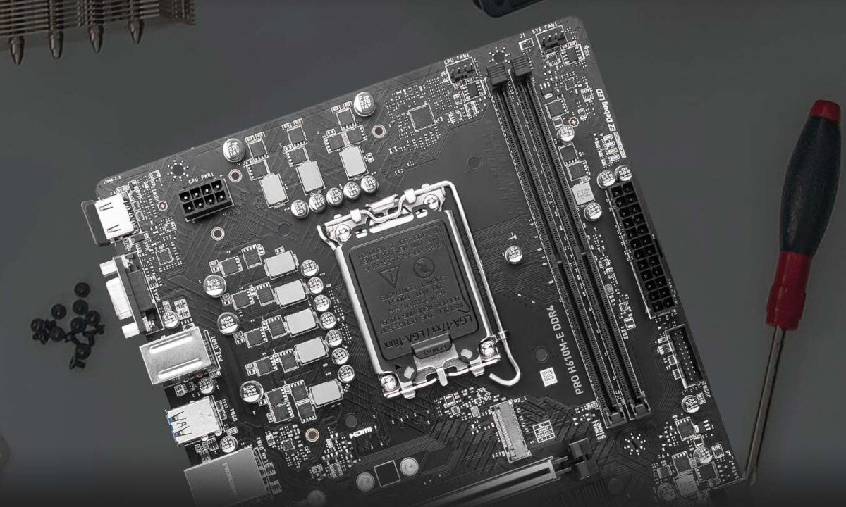 Na obrazie widoczna jest płyta główna z oznaczeniem \'PRO H610M-E DDR4\', otoczona przez kilka śrubek i śrubokręt. Płyta posiada różne złącza i komponenty elektroniczne.