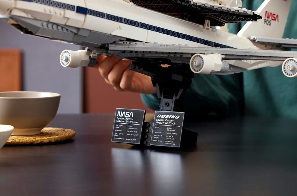 Model samolotu z klocków LEGO z widocznymi tabliczkami informacyjnymi z napisami: \'NASA Space Shuttle Orbiter Enterprise\' oraz \'BOEING Shuttle Carrier Aircraft N905NA\'.