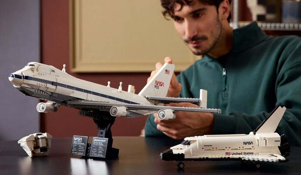 Osoba składa model samolotu z klocków LEGO z widocznym logo NASA i napisem \'905\'. Obok znajduje się model wahadłowca z napisem \'United States\'.