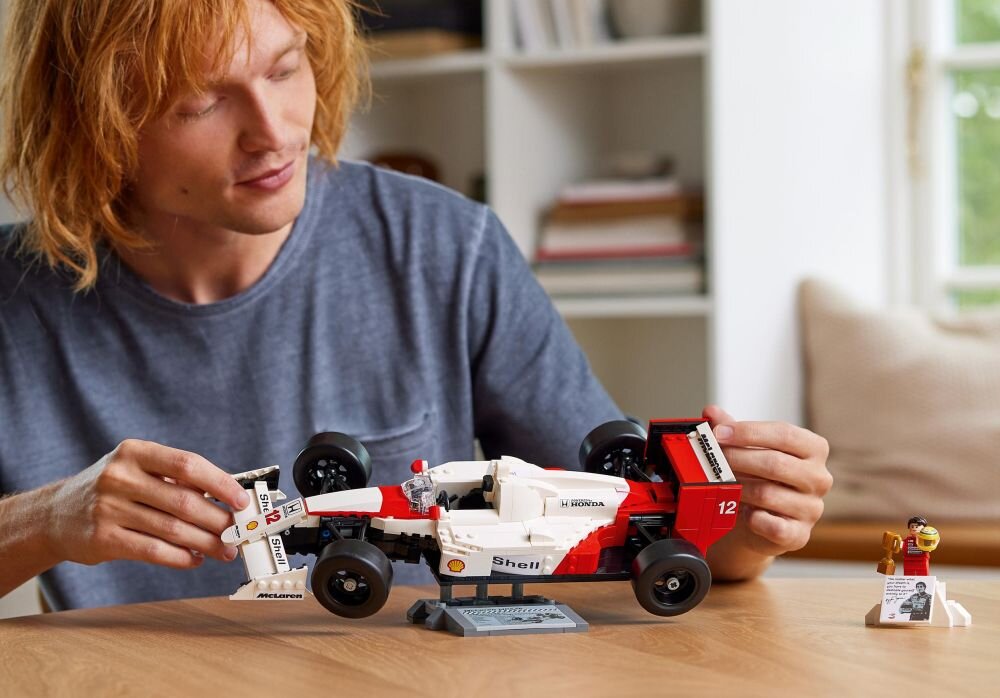 Osoba trzyma model samochodu wyścigowego z klocków LEGO, z widocznymi logotypami Shell, Honda i McLaren. Obok znajduje się mała figurka z tabliczką.