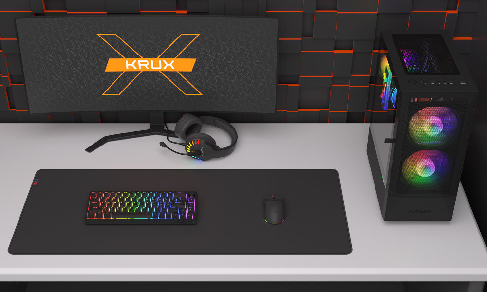 Na biurku znajduje się monitor z logo KRUX, klawiatura, myszka, słuchawki oraz komputer z obudową z podświetleniem RGB. Wszystkie elementy mają nowoczesny design i są ustawione na dużej podkładce.