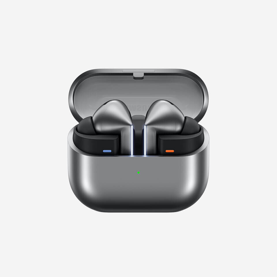 Galaxy Buds3 Pro Srebrne słuchawki douszne w etui ładującym z otwartą pokrywą, z widocznymi niebieskim i pomarańczowym akcentem na słuchawkach. Na etui znajduje się zielona dioda LED.