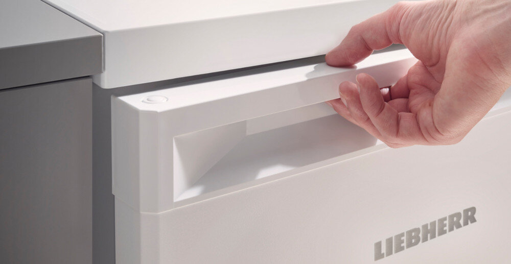 Osoba otwiera białą lodówkę z widocznym logo LIEBHERR na drzwiach.