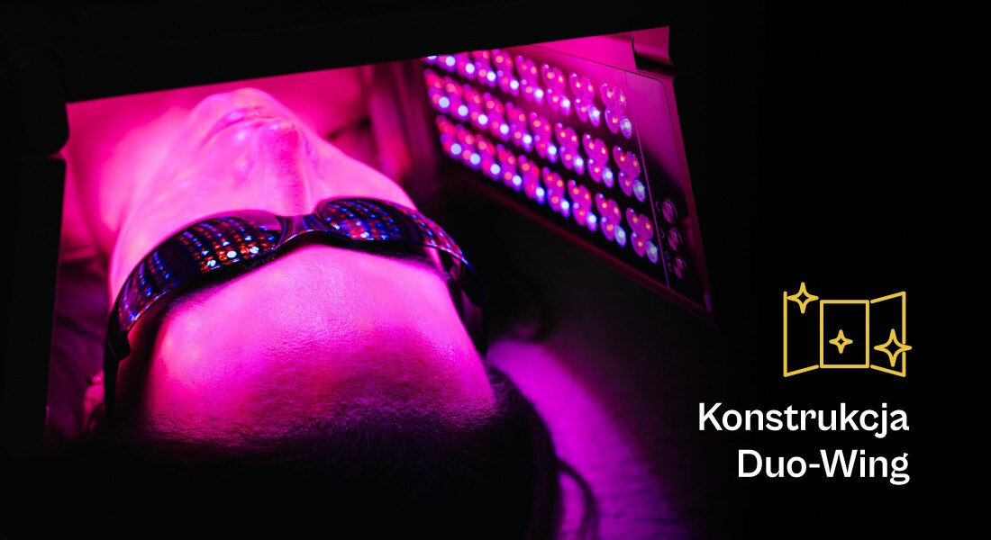 Osoba leży pod panelem LED emitującym różowe światło, nosząc okulary ochronne. Obok znajduje się napis \'Konstrukcja Duo-Wing\' z ikoną przedstawiającą otwarte drzwi z gwiazdkami.