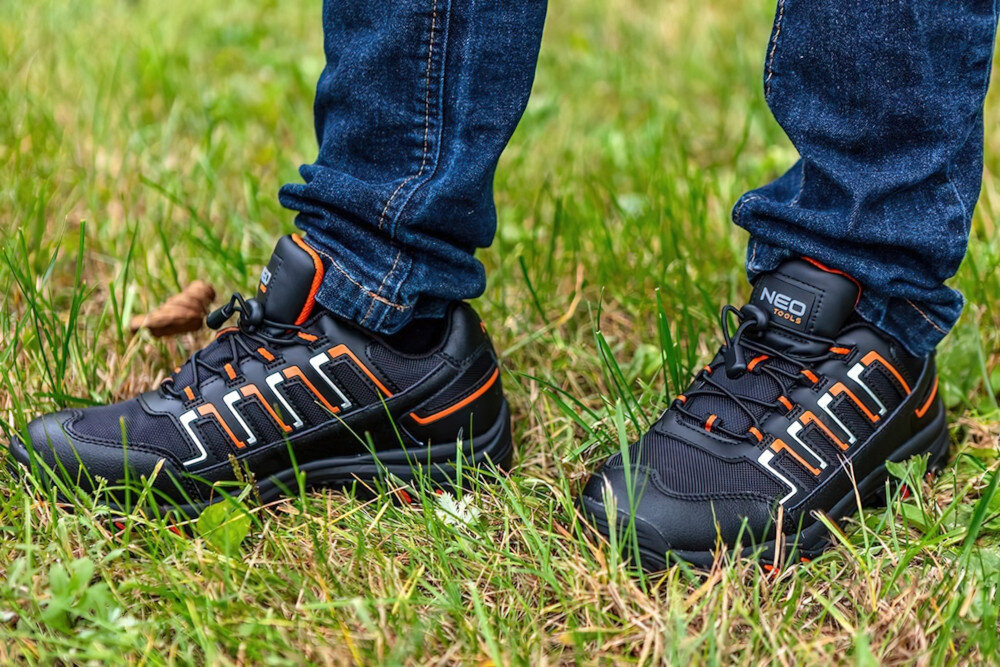 Półbuty robocze NEO TOOLS 82-715 rozmiar 44 osoba stoi na trawie buty widoczne od przodu pod skosem bezpieczeństwo w pracy ochrona stóp wysoka jakość wygodne stabilne