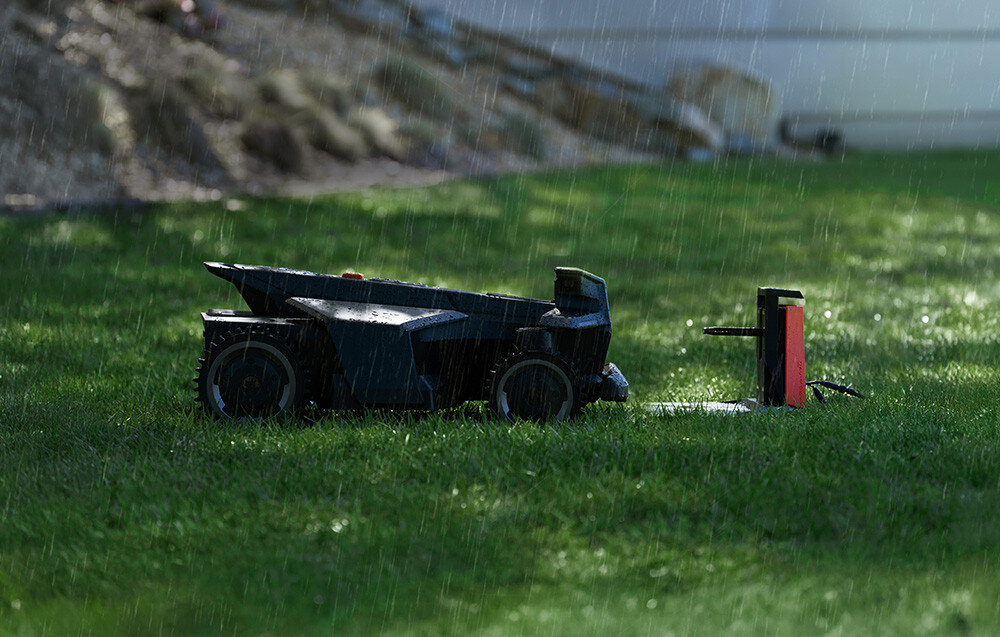 Na trawie widać robot koszący podczas deszczu. W tle znajduje się niewyraźny krajobraz z roślinnością.